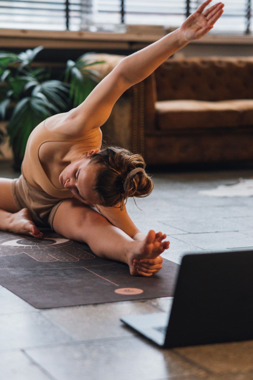 A student practising a seated side stretch at home in front of a laptop