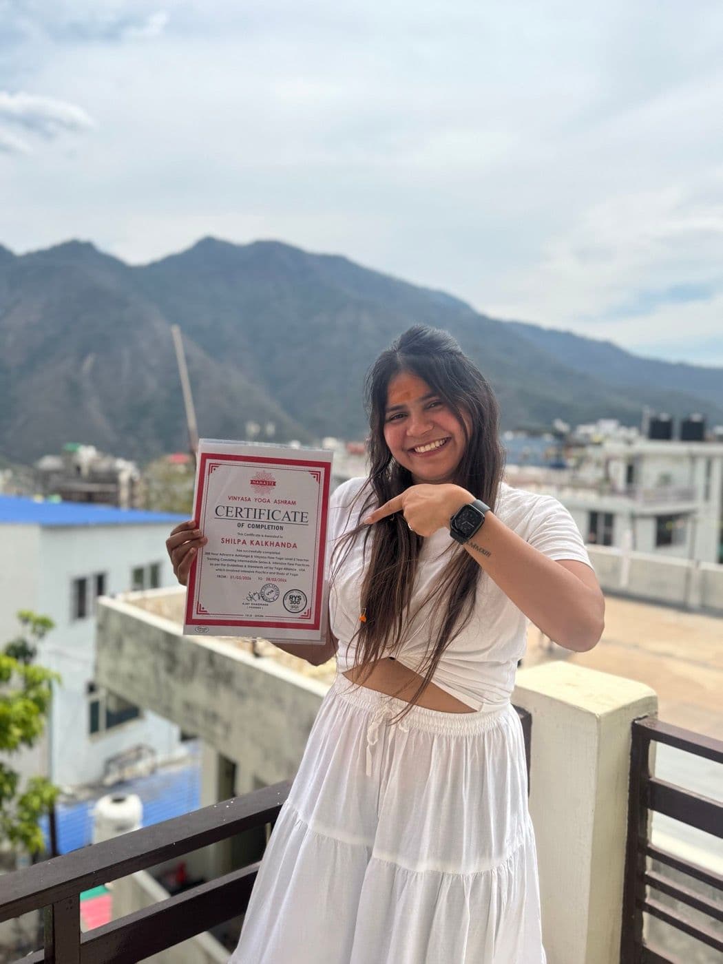 Shilpa with her Yoga Alliance certification, mountains behind